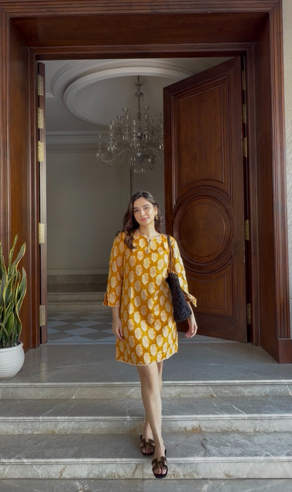 Woman in a yellow dress standing in front of a wooden door with a chandelier inside.