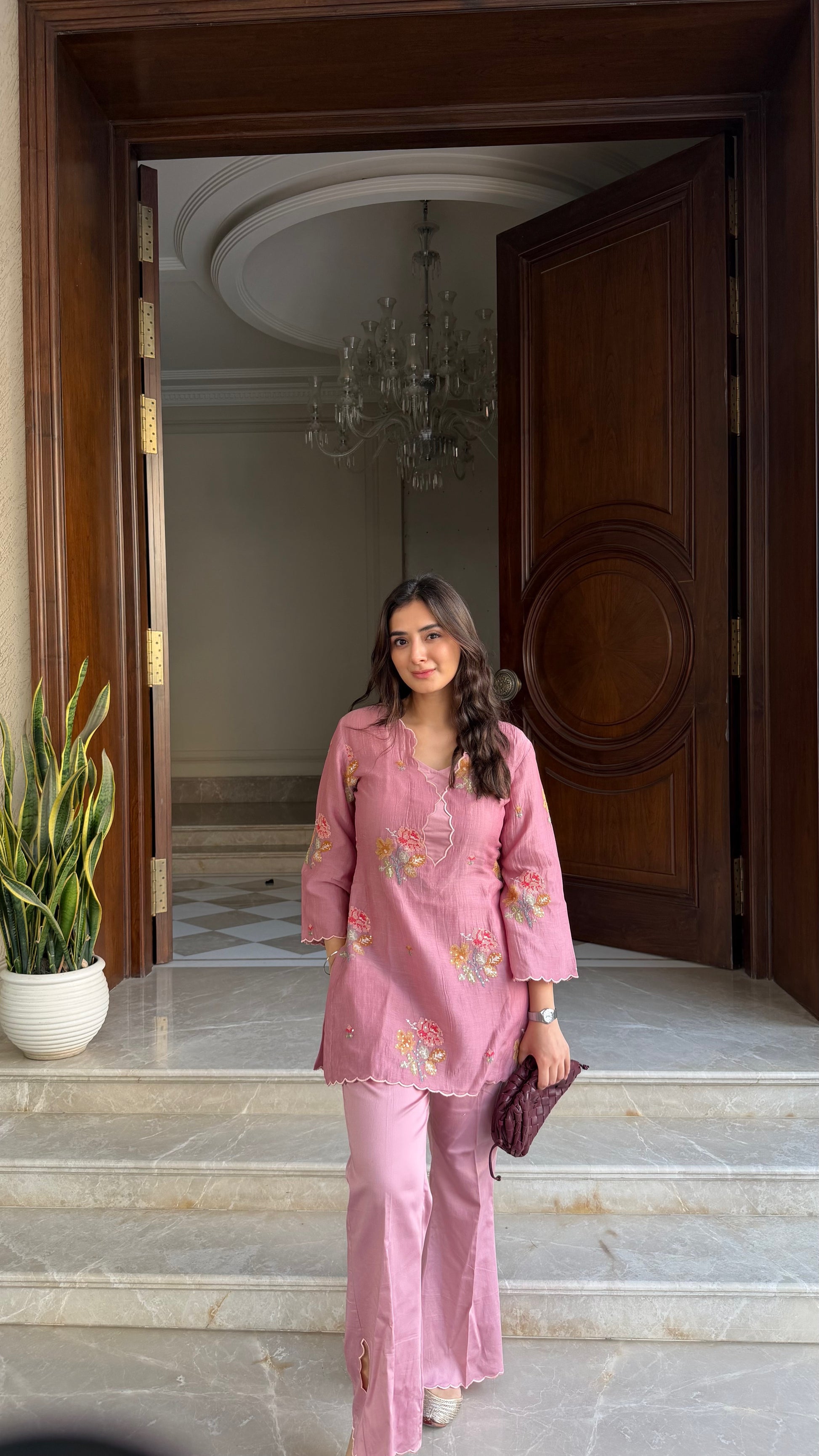 Woman in a pink outfit standing in front of a large wooden door.
