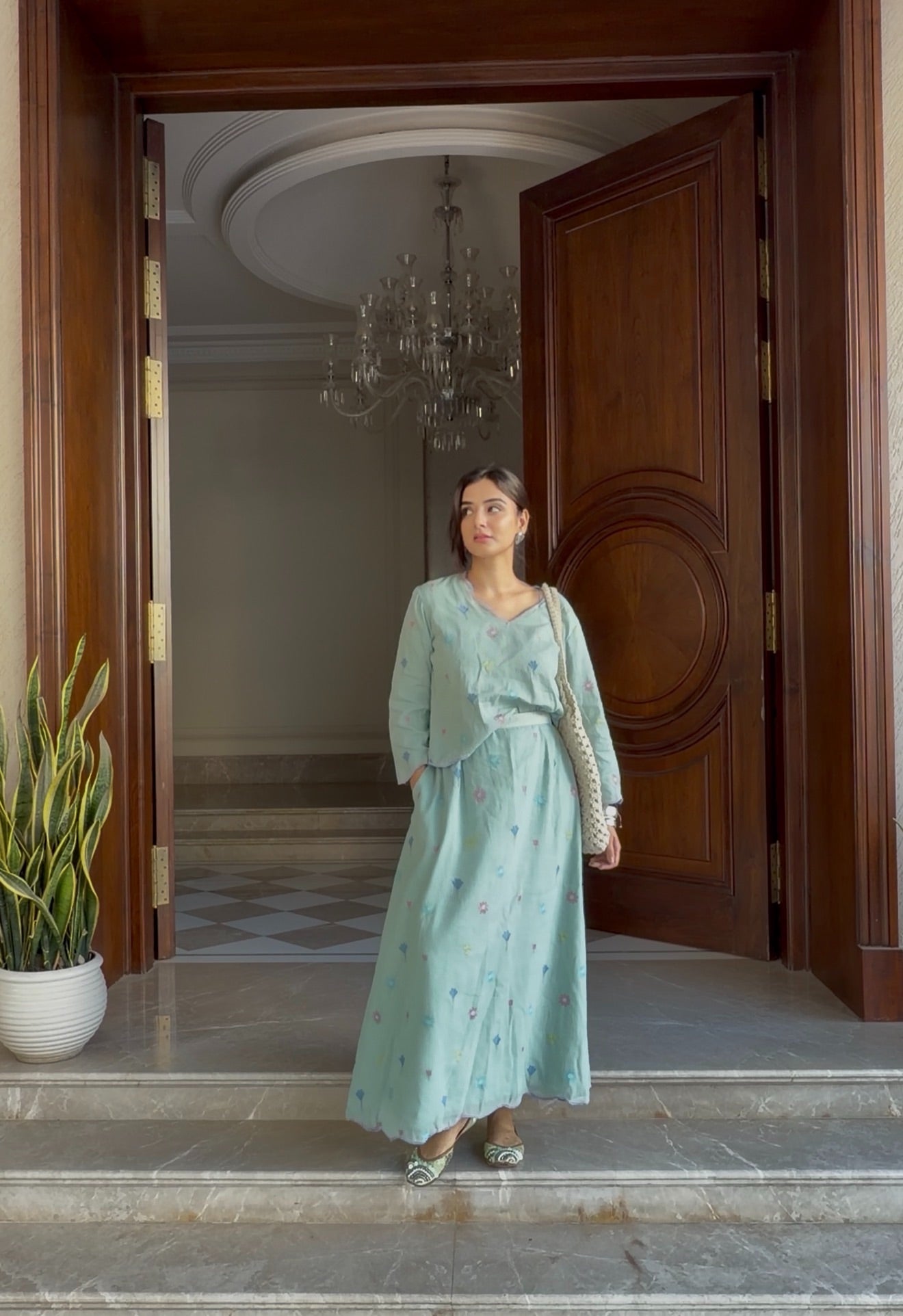 Woman in a light green outfit standing in a doorway with a chandelier in the background